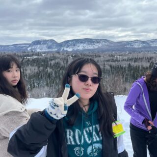three-international-students-snowshoeing-on-top-of-hill-looking-at-camera-holding-peace-sign