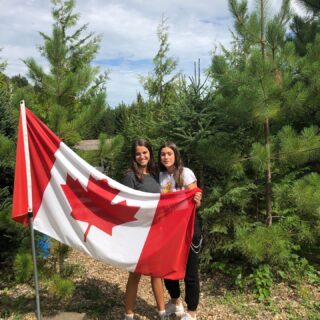 two-international-students-holding-canadian-flag-with-trees-behind-them
