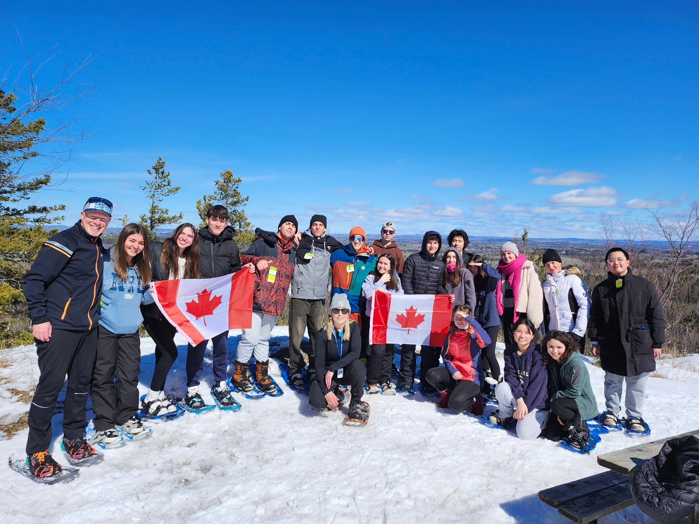 group-of-international-students-with-snowshoes-on-top-of-hill-holding-canadian-flags